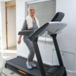 Active senior woman in sportswear using treadmill at home. Coronavirus Covid19 social distance. Home workout, active seniors, stay at home concept.